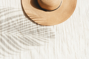  Straw hat and palm leaf shadow on beige linen cloth material background