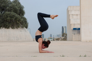 Young middle eastern woman standing on her forearms. Shot in an empty urban park with Tel Aviv buildings in the far background.