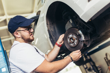 Professional near the car hanging on the lift at the service station make a diagnostics, repair the...