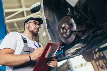 Professional near the car hanging on the lift at the service station make a diagnostics, repair the brakes