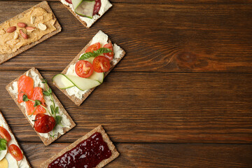 Fresh rye crispbreads with different toppings on wooden table, flat lay. Space for text