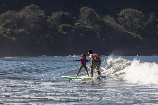 Young 5 year old girl rides wave with father 