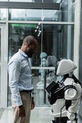 african american engineer looking at humanoid robot in office