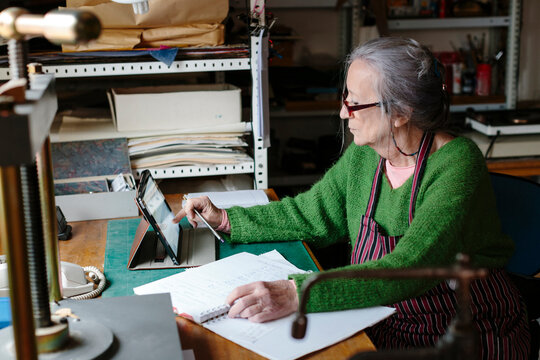 Elderly woman using electronic device sitting by a desk in a workshop
