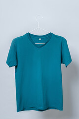 Worn blue t-shirt hanging on a hanger against gray background