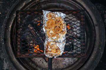 Onions are grilled on the foil over a campfire.