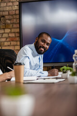 successful african american businessman smiling at camera near lcd monitor in conference room