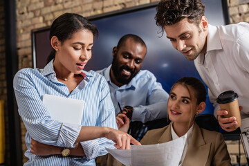 african american businesswoman pointing at documents near smiling coworkers