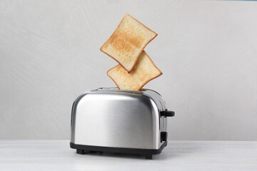 Bread slices popping up from modern toaster on white wooden table