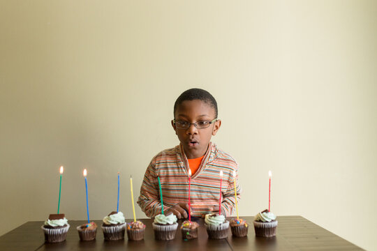 Black boy blows out candles on birthday cupcakes.