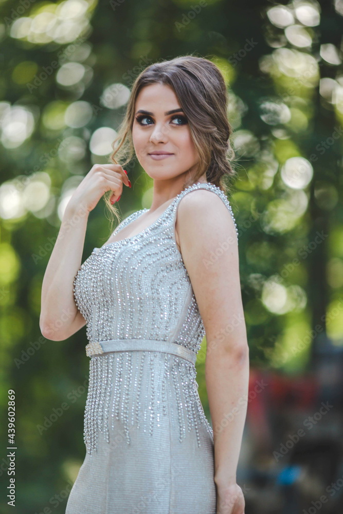 Wall mural pretty caucasian woman with a silver evening dress and heavy makeup posing in the park