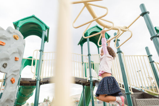 Smiling girl hangs from playground bars