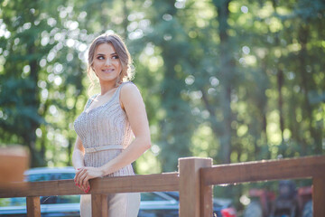 Pretty Caucasian woman with a silver evening dress leaning on wooden handles and posing