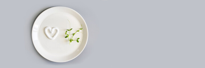 Heart shape cream. Beauty lotion. Mayonnaise smear on white plate. Top view with copyspace. White product smear. Valentine concept. Horizontal banner. Green peas. Grey background