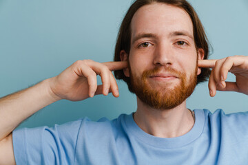 Young ginger man with beard plugging his ears and looking at camera