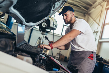 Fototapeta na wymiar Professional car mechanic working in auto repair service using laptop.