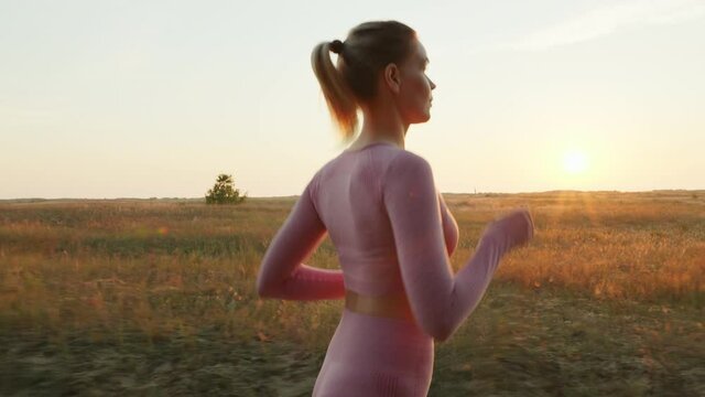 Lifestyle Young Woman Athlete Running lens flares in pink Sportswear Jogging rejoices against blue sky at sunrise summer. Human endurance test. Competition or marathon. Sport dawn workout 
