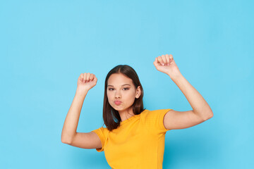 woman in a yellow t-shirt and raised her hands up on a blue background cropped view