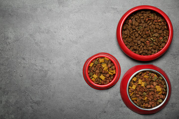 Pet bowls with dry food on grey background, flat lay. Space for text