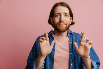 Young ginger man with beard holding finger crossed for good luck