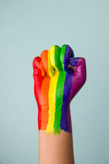 Photo of a raised fist colored with the rainbow color for lgbtq community.