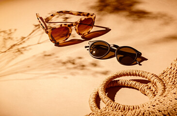 2 pairs of women sunglasses and a bag on a soft orange background and strong shadows of flowers - Powered by Adobe