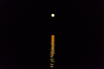Full moon in the distance in complete darkness with reflection in the distance.