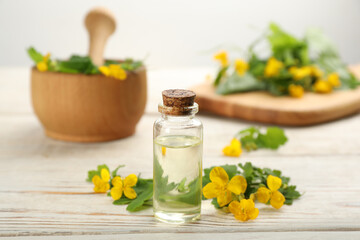 Bottle of natural celandine oil near flowers on white wooden table