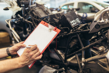Man writing on a clipboard in a garage. Professional motorcycle mechanic working in bike repair...