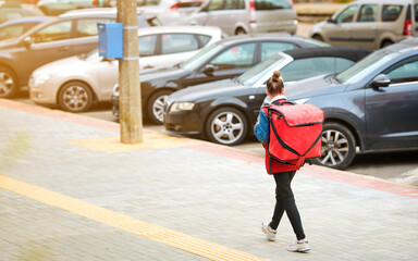 Woman delivers food and pizza in red backpack. Fast delivery of goods, food delivery service. Delivery Woman carrying thermal bag. Young female courier walking along street. Online shopping concept