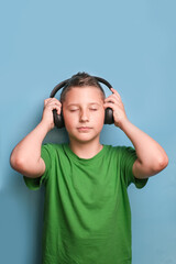 Headshot of boy in earphones listening to music and relaxing with closed eyes. Portrait on blue background 