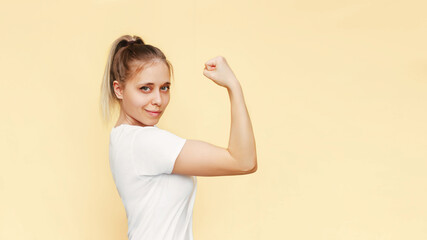 Strong powerful confident caucasian young blonde woman raises arm and shows bicep isolated on a...