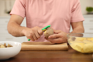 Obraz na płótnie Canvas Man peeling potato at table, closeup. Preparing vegetable