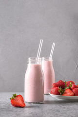 Traditional ayurvedic healthy Indian strawberry lassi or milkshake in two bottle on gray background. Vertical format.