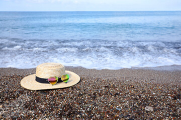 Fototapeta na wymiar Straw hat and colorful heart shaped sunglasses on sea beach. Space for text