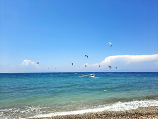 Kiteboarders catch the wind in the Rhodos, Greece. Aegean Sea. Extreme water sport. Group of kiteboarding is flying in the blue sky by the wind blow.