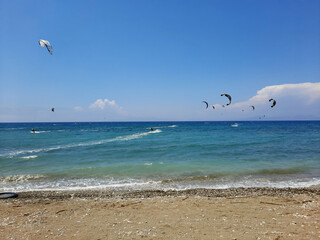 Kiteboarders catch the wind in the Rhodos, Greece. Aegean Sea. Extreme water sport. Group of kiteboarding is flying in the blue sky by the wind blow.