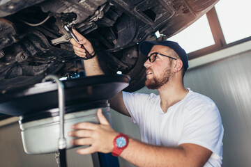 Portrait of a mechanic repairing a car in his garage, oil change.