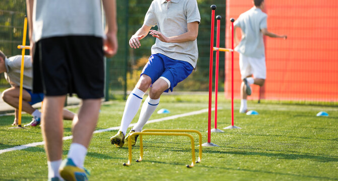 Teenage Football Players on Training Camp. Young Boys Running Slalom Track Between Training Poles and Jumping Over Hurdles. Soccer Training Equipment