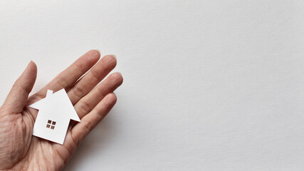 A man holds a paper house in his hand. The symbol of the purchase of housing