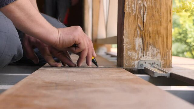Repair home. Flooring installation a terrace. Carpenter draws a cutting line on wood plank. Close up measuring floorboards with corner ruler. Joiner with pencil and meter marks measure on wooden board
