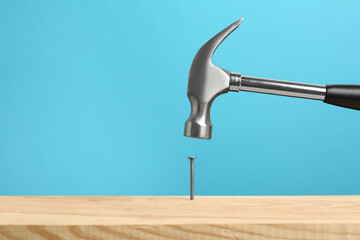 Hammering nail into wooden surface against light blue background