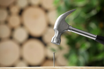 Hammering nail into wooden surface against blurred background