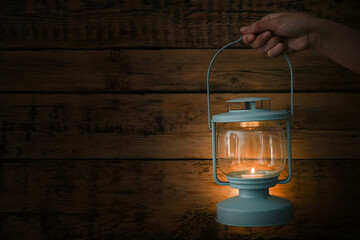 Woman holding lantern with burning candle against wooden wall in darkness, closeup. Space for text