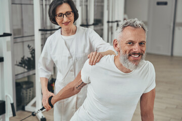 Handsome pleased man enjoying his strength workout with a kinesiologist