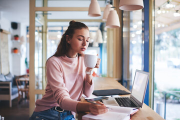 Fototapeta premium Calm student writing and drinking coffee in coffee shop