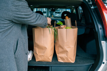 man putting bags with product in car trunk