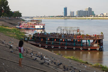 A barefoot little girl watches the boats moored at the mouth of the Tonle Sap River on the Mekong...