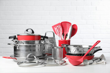 Set of clean kitchenware on white table against brick wall