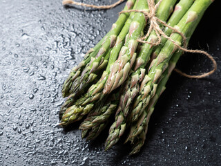 Raw green asparagus on wet black slate background